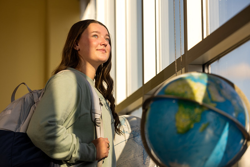 student standing in classroom with globe in the foreground