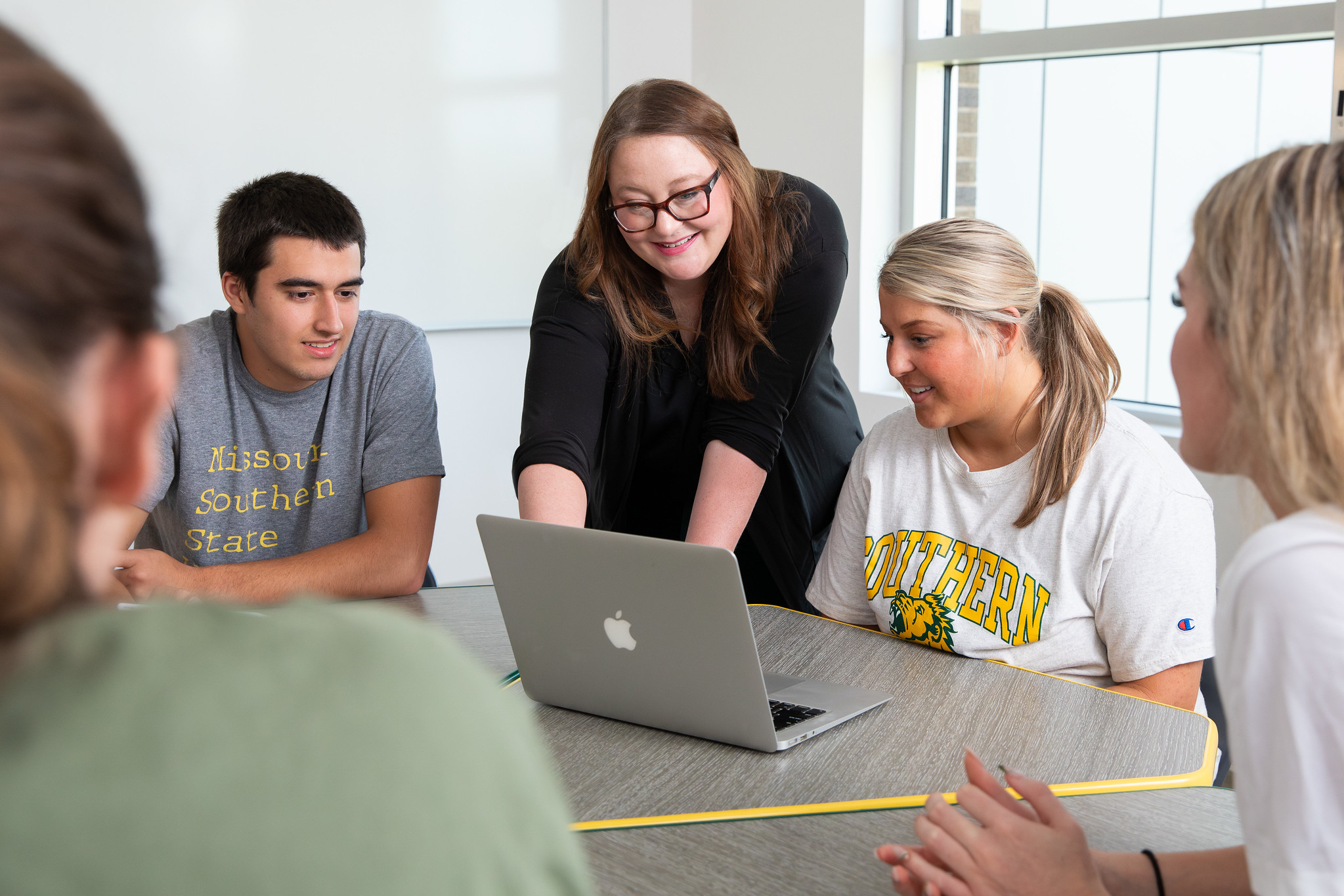 students gathered at table listening to faculty member 