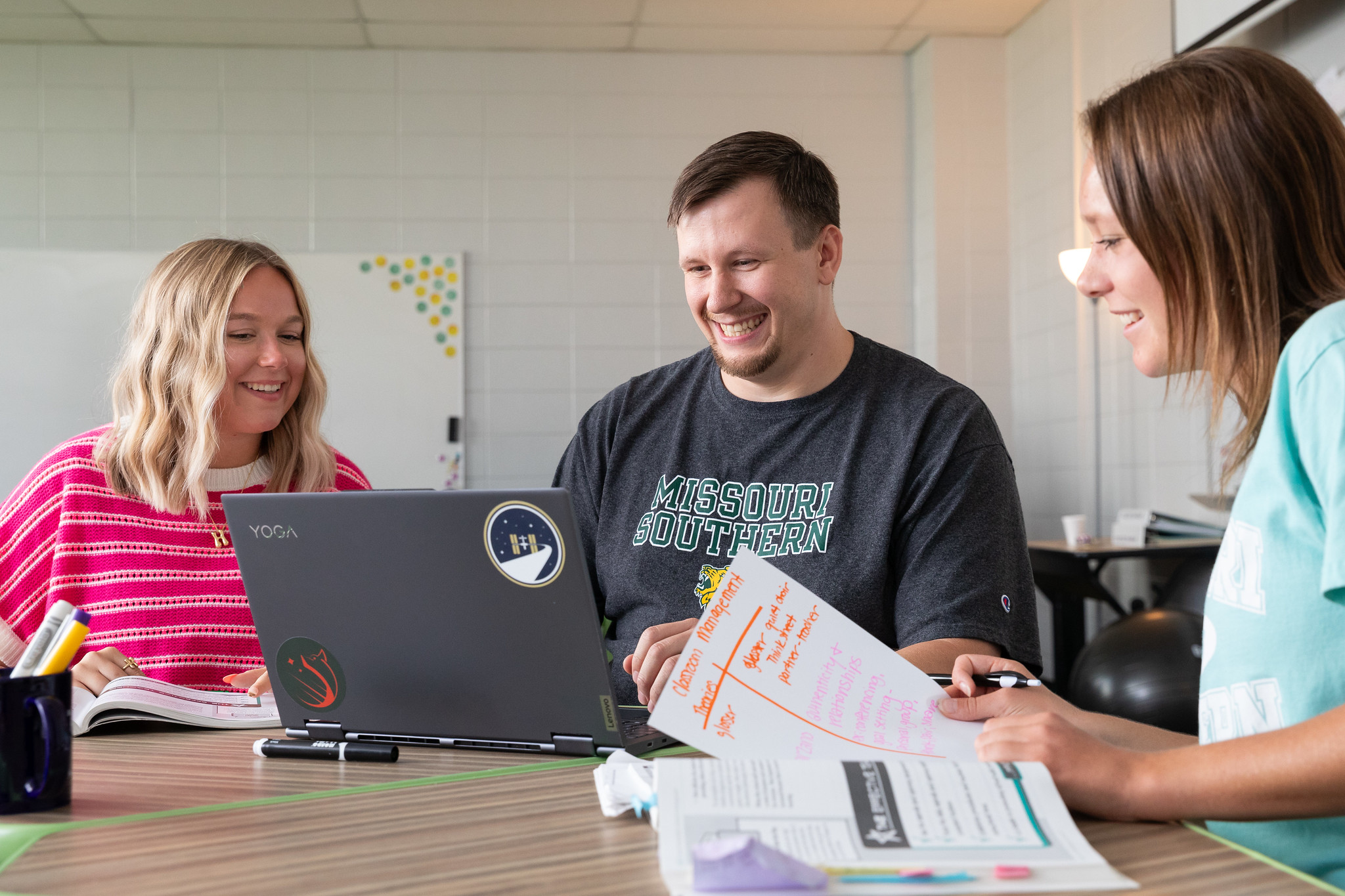students sitting at table with laptop and study materials 