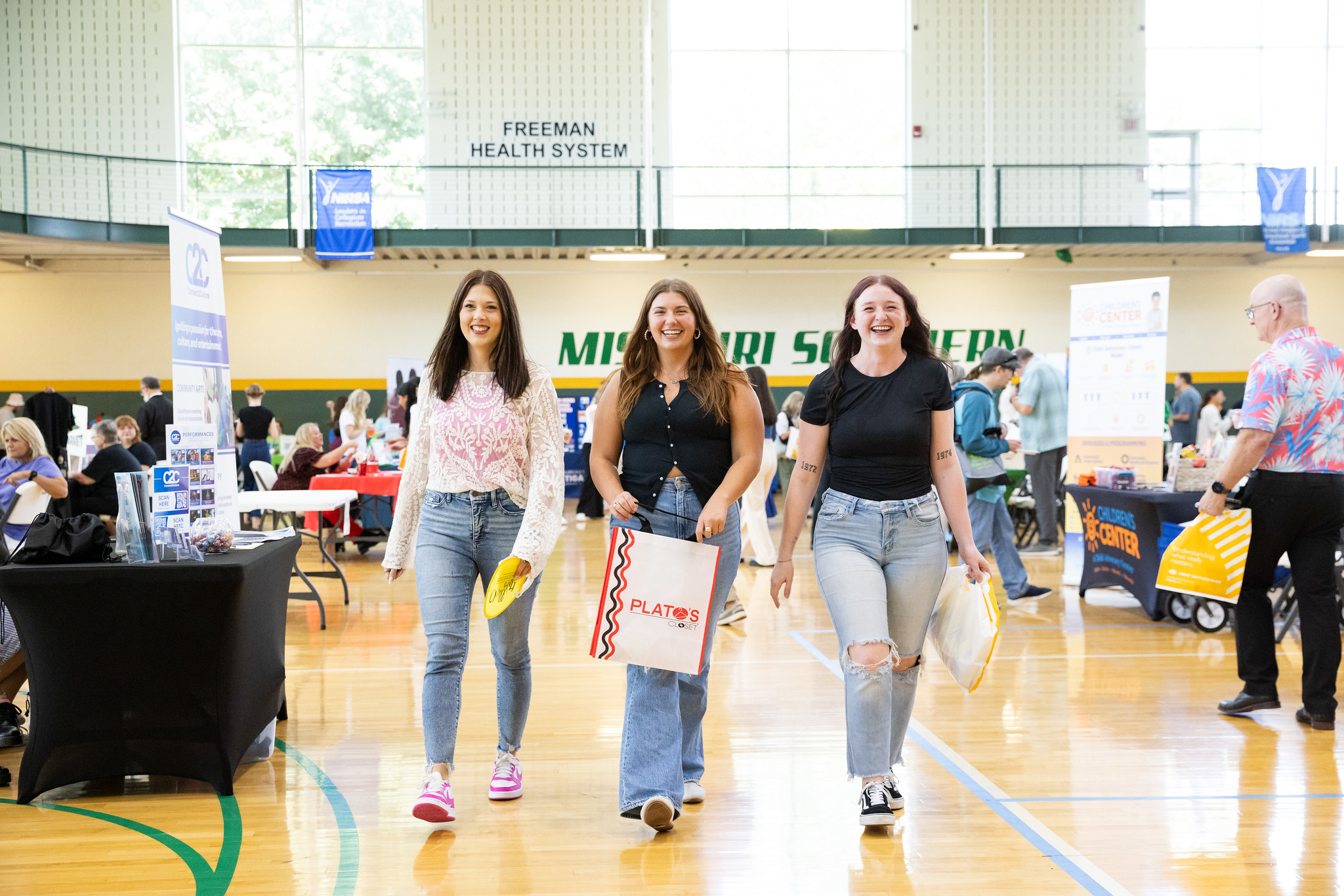 three individuals standing in gym smiling at camera with bags in hand 